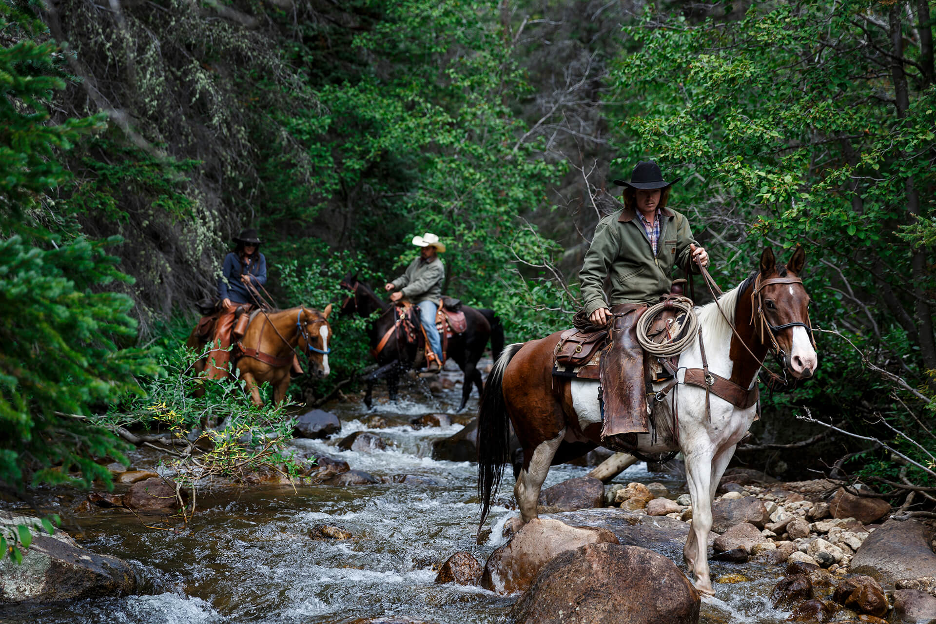 People riding horses with cowboy hates during a western vacation at Rawah Ranch